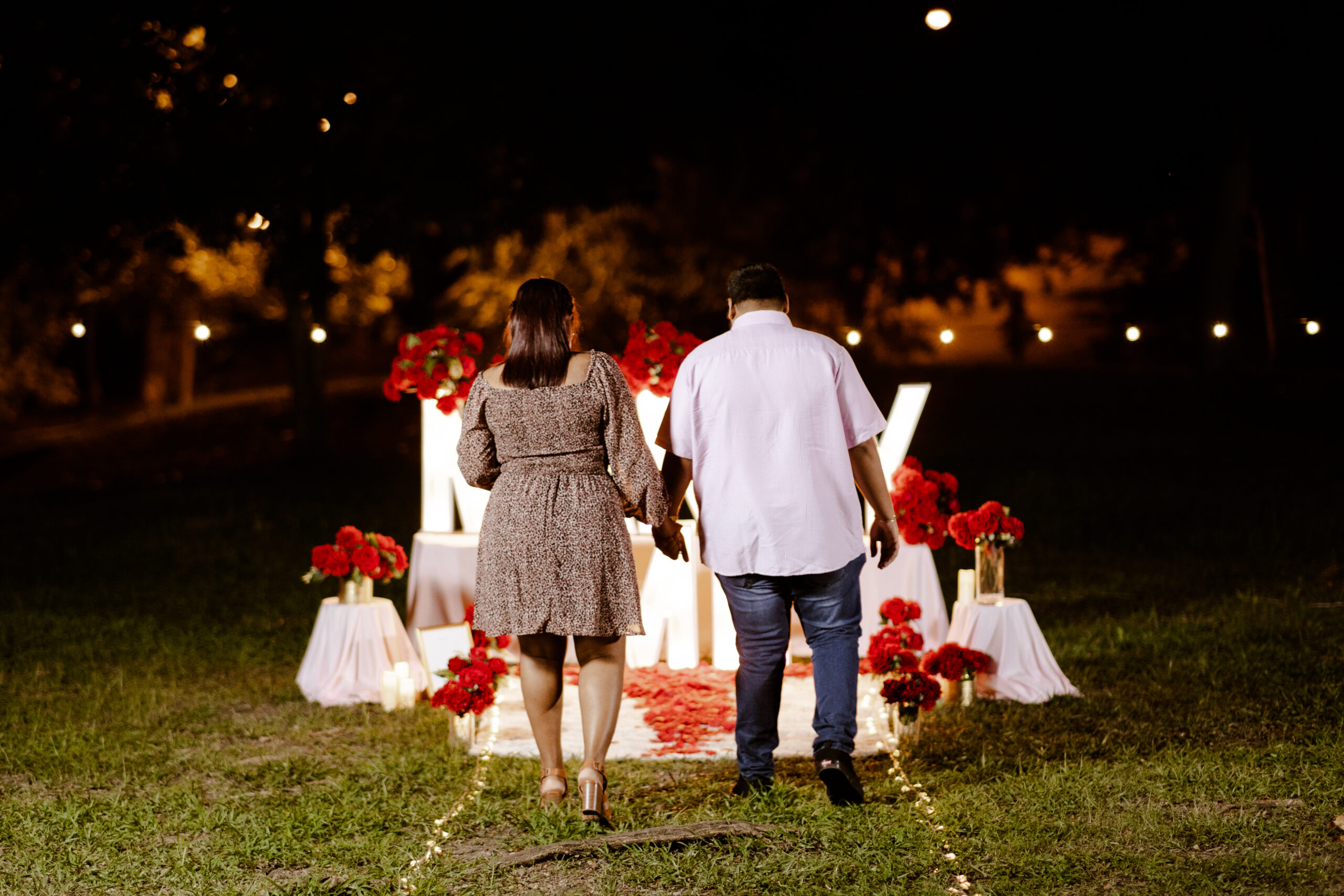 romantic proposal couple walking handing in hand towards marry me letters